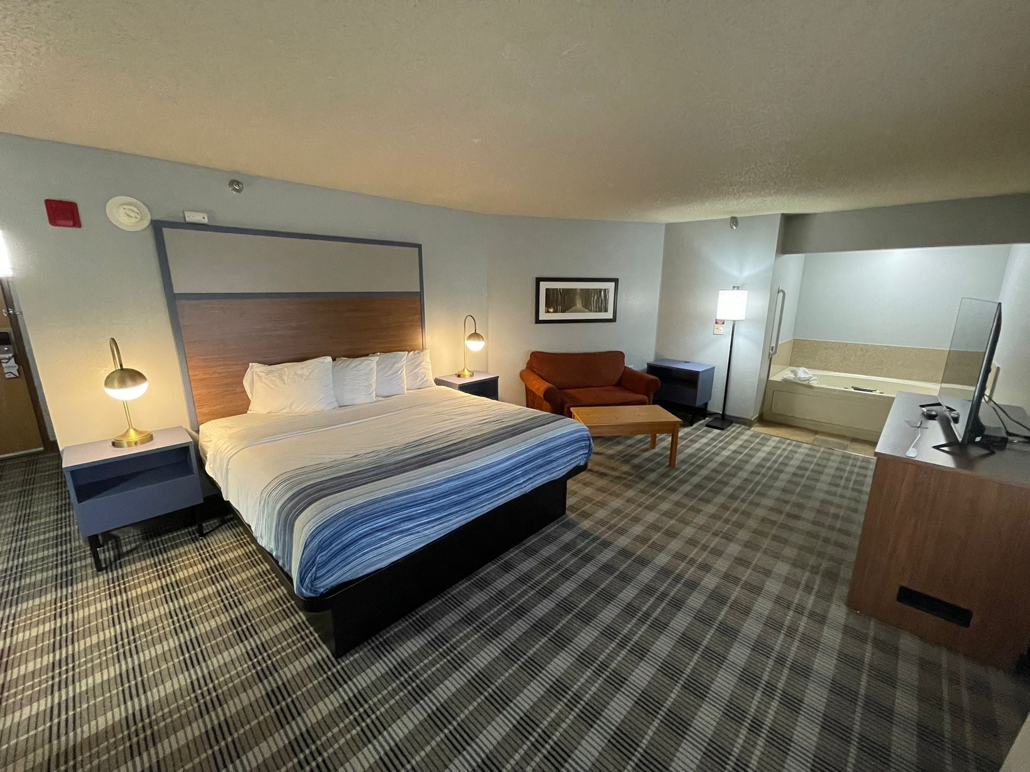 Une chambre d’hôtel avec un grand lit, un bureau, une chaise, une lampe de bureau, une table de chevet et un téléviseur fixé au mur.