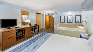 A hotel room with a bed, a desk with a TV, a microwave, a chair, a desk lamp, a vanity with a mirror, and framed pictures on the wall. - AmericInn by Wyndham Sayre (Sayre)