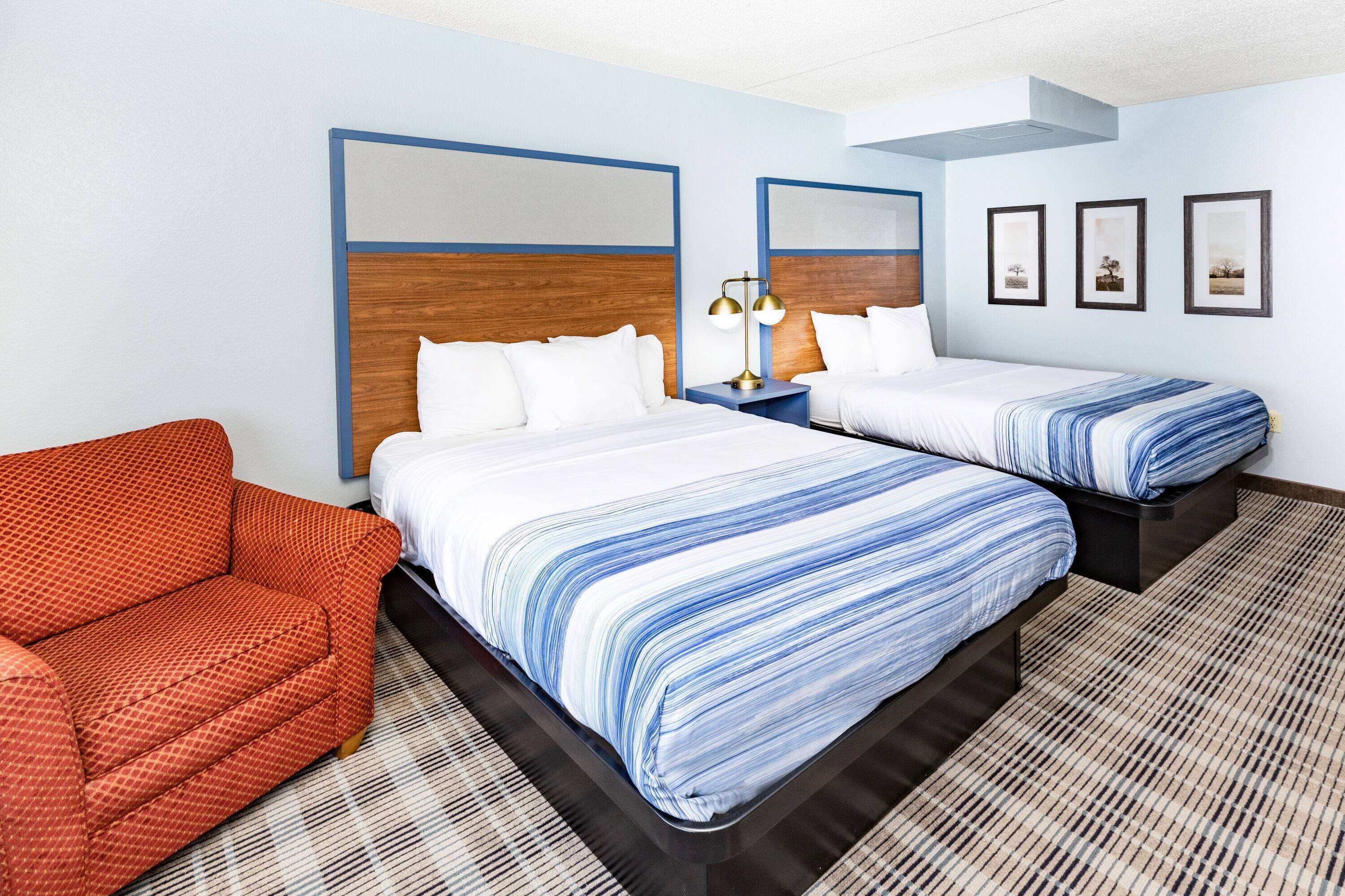 Una habitación de hotel con dos camas, un sofá y una mesita de noche con lámpara.