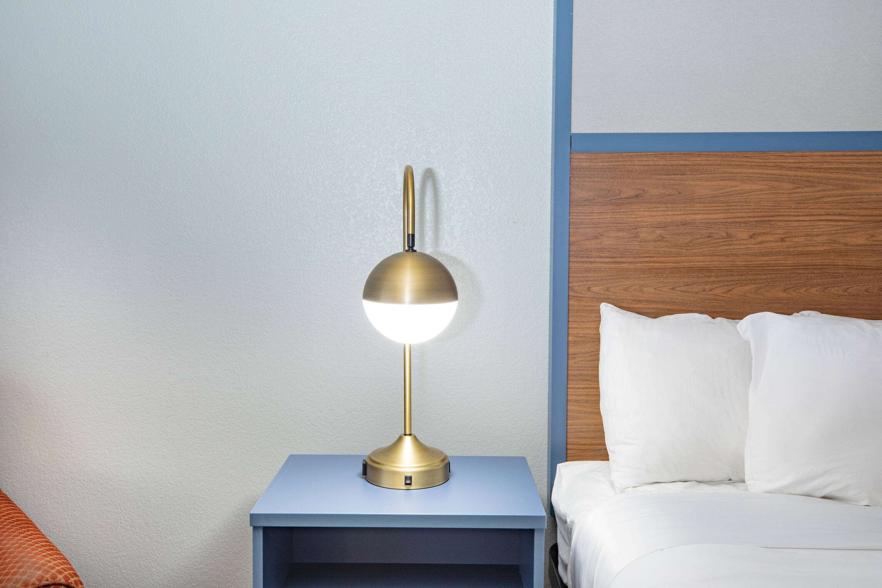Ein Nachttisch mit Lampe, ein Bett mit weißer Bettwäsche und ein hölzernes Kopfteil.