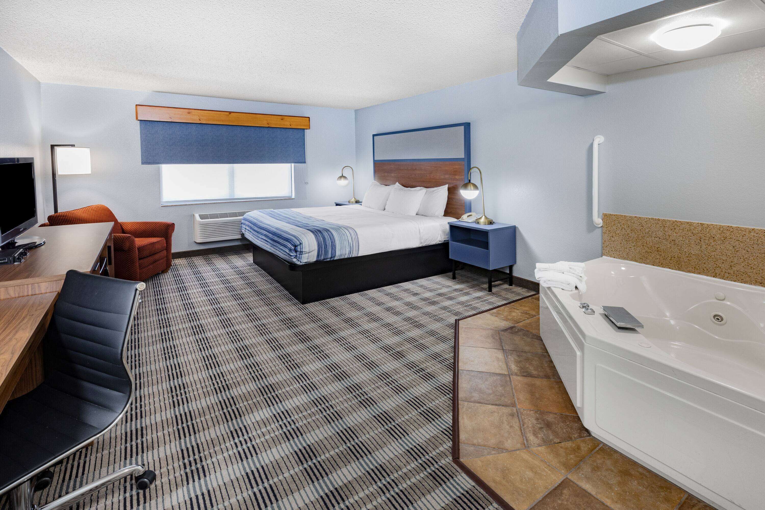 Una habitación de hotel con cama, escritorio, silla y baño independiente con bañera.
