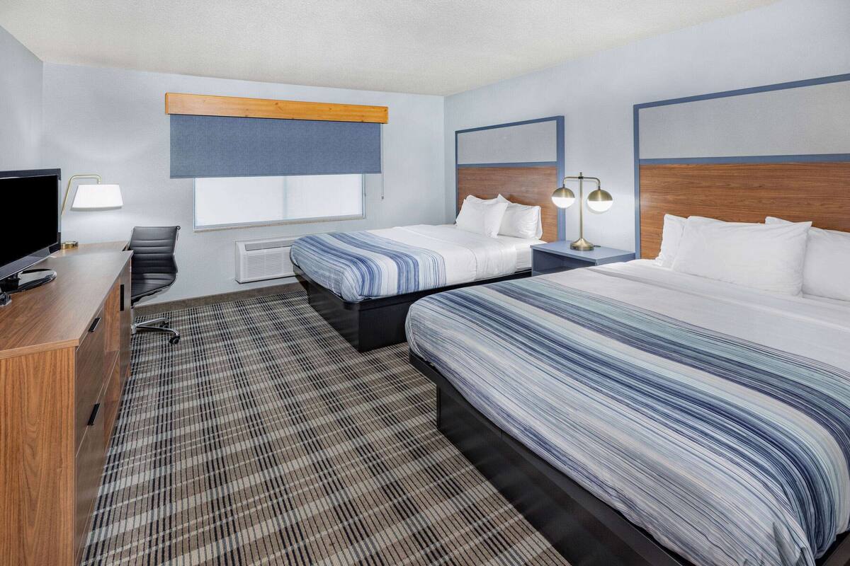 A hotel room with two beds, a desk with a TV, a chair, and a window with a blind.
