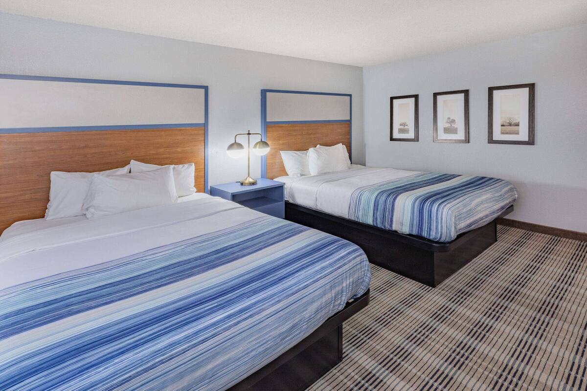 A hotel room with two beds, a nightstand with a lamp, and three framed pictures on the wall.