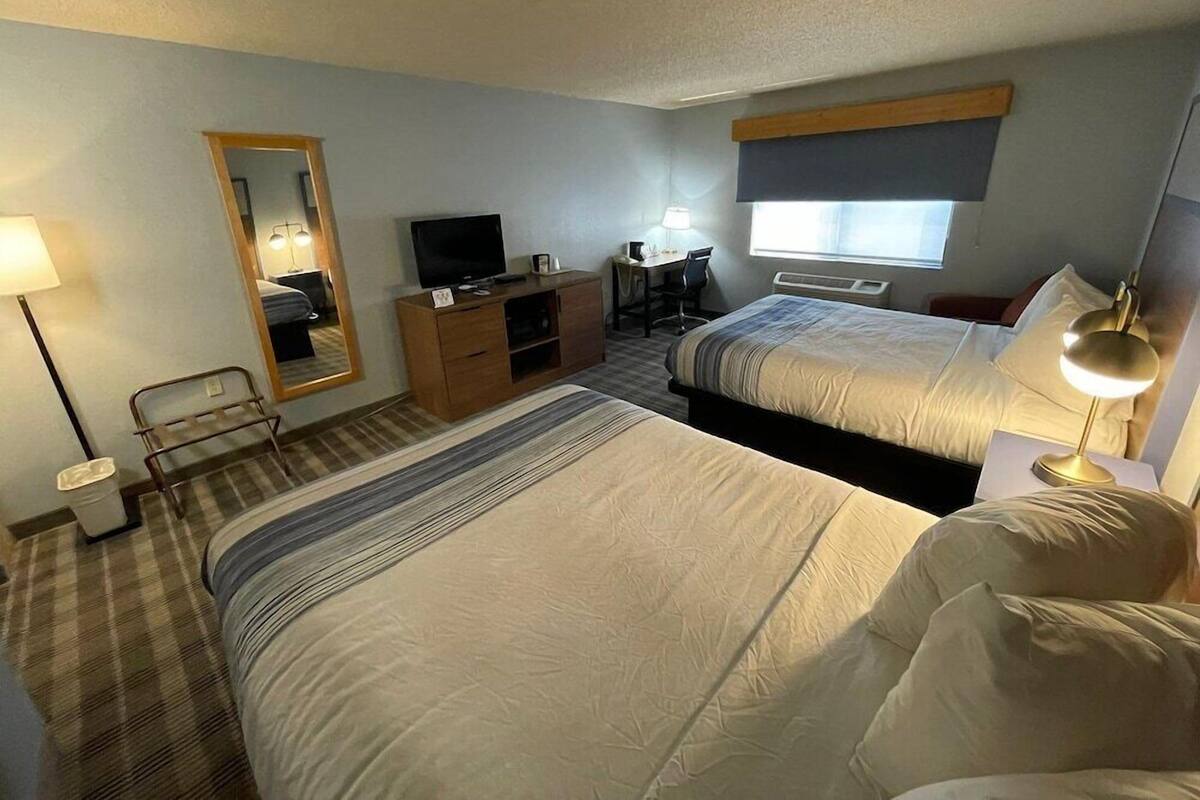 A hotel room with two beds, a desk, a chair, a television, a mirror, and a window.