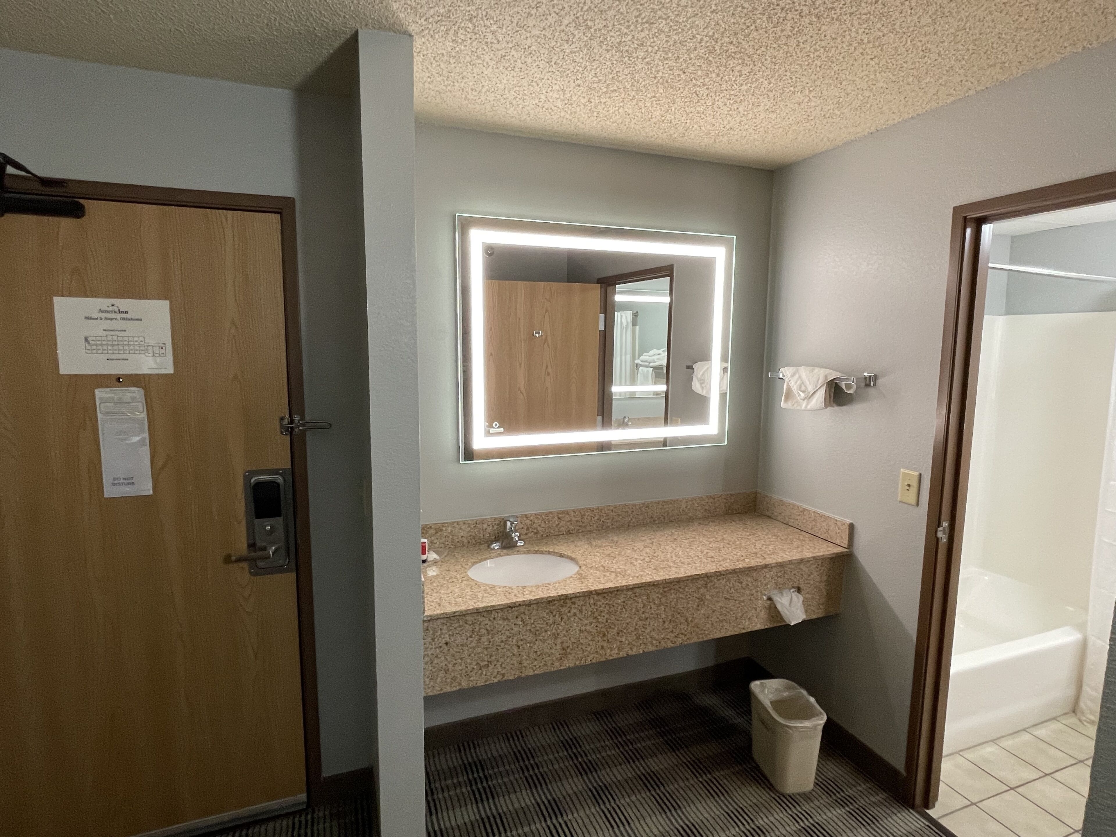 Un baño con puerta de madera, un lavamanos con espejo y un cubo de basura.