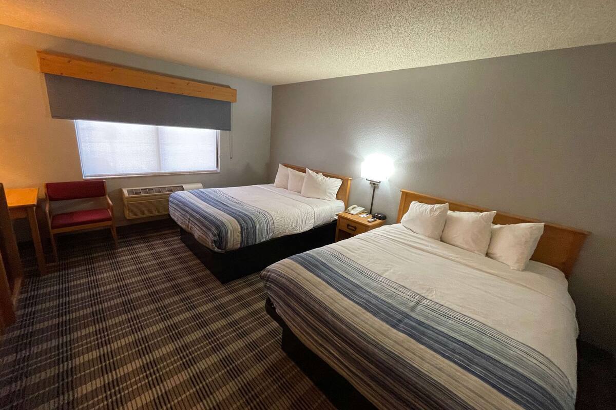 A hotel room with two beds, a desk, a chair, and a window.