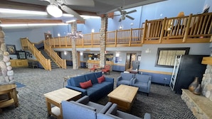 A spacious lobby with a high ceiling, a wooden staircase, and a second-floor balcony. - AmericInn by Wyndham Sayre (Sayre)