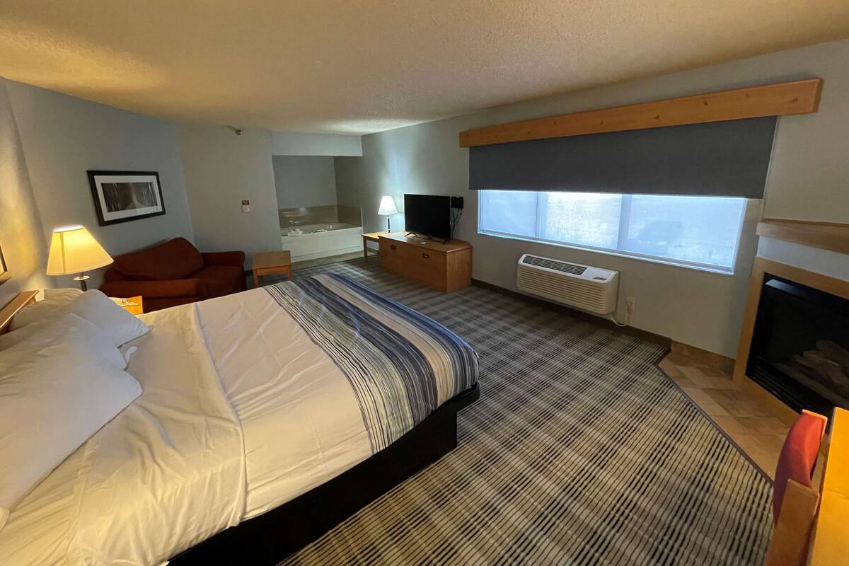 A hotel room with a bed, a TV, a desk, a chair, a window, and a fireplace.