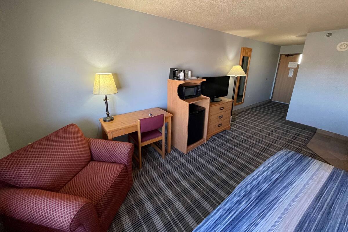 A hotel room with a bed, a desk with a computer, a TV, a microwave, and a chair.