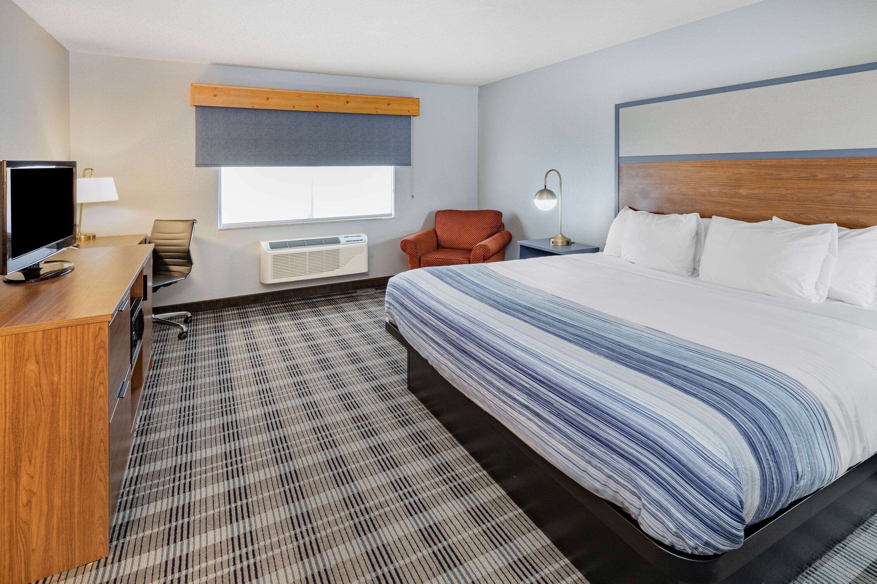 A hotel room with a large bed, a desk with a TV, a chair, a lamp, and a window.