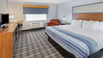 A hotel room with a large bed, a desk with a TV, a chair, a lamp, and a window.