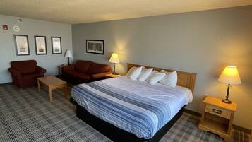 Una habitación de hotel con una cama grande, dos mesitas de noche, un tocador de madera, un sillón rojo, un sofá marrón y un mueble de madera pequeño.