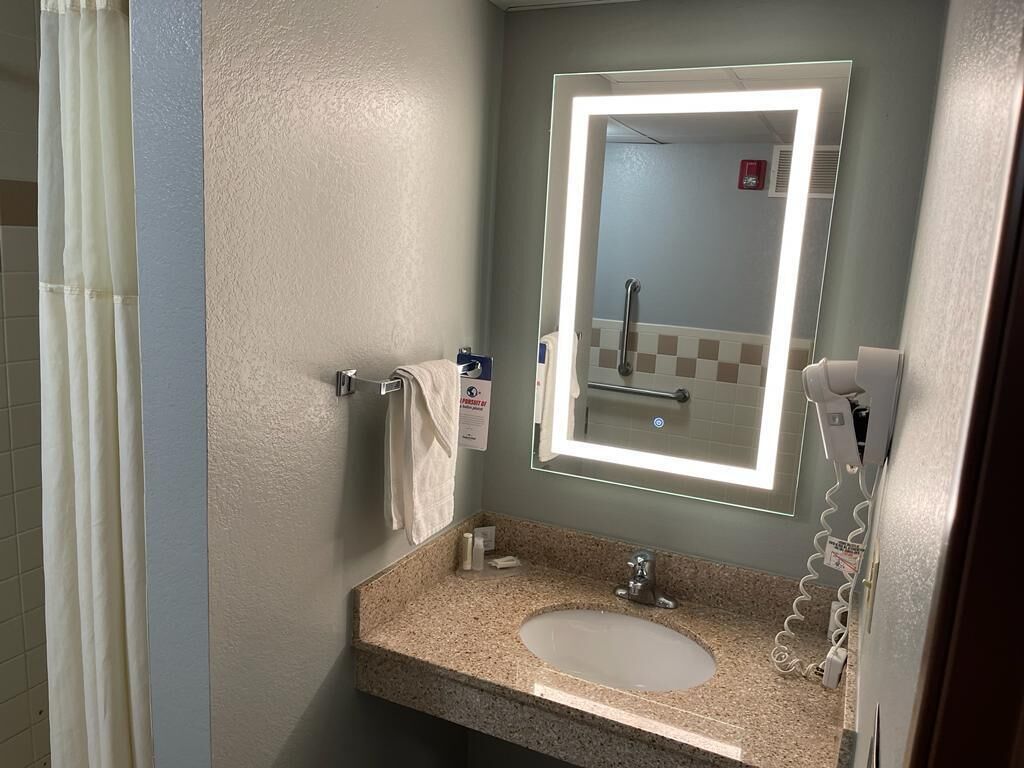 A bathroom with a granite countertop sink, a mirror with a light, a towel rack, and a hand dryer.