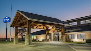 A hotel entrance with a covered outdoor area, stone pillars, and a clear sky. - AmericInn by Wyndham Sayre (Sayre)