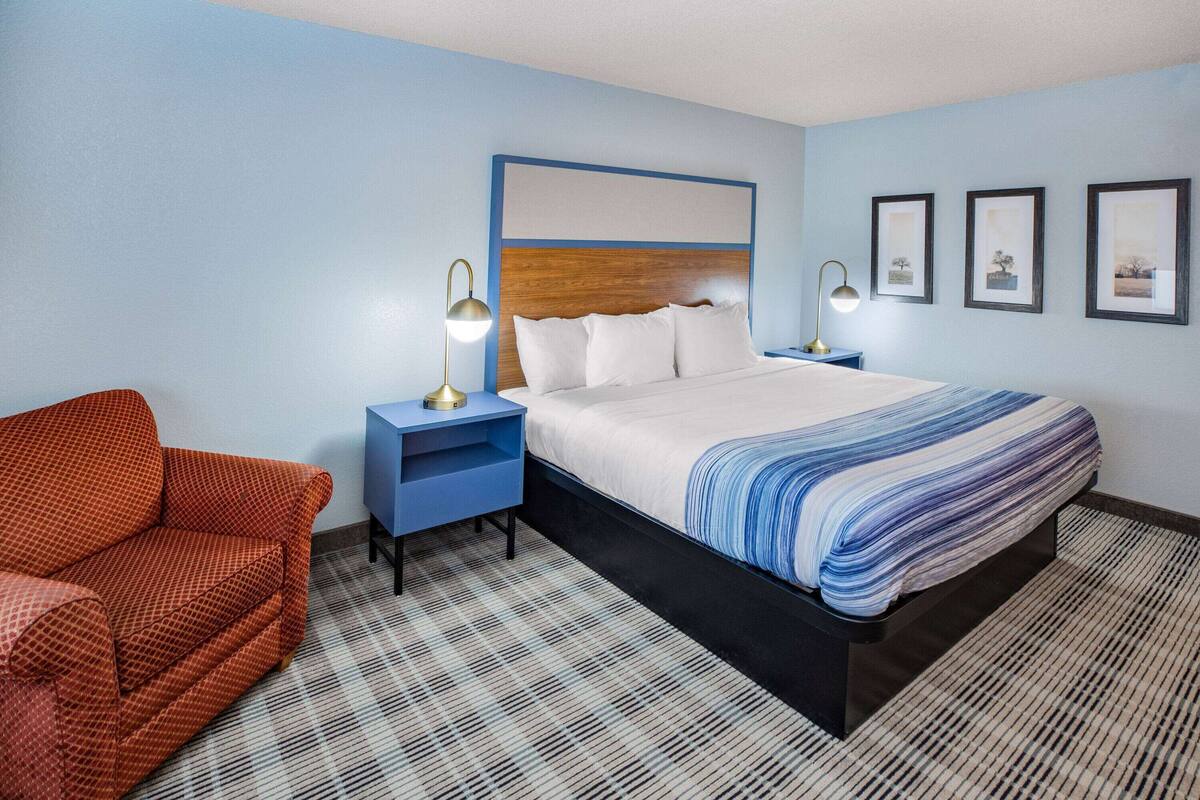 A hotel room with a bed, two nightstands, a red sofa, and a patterned carpet.
