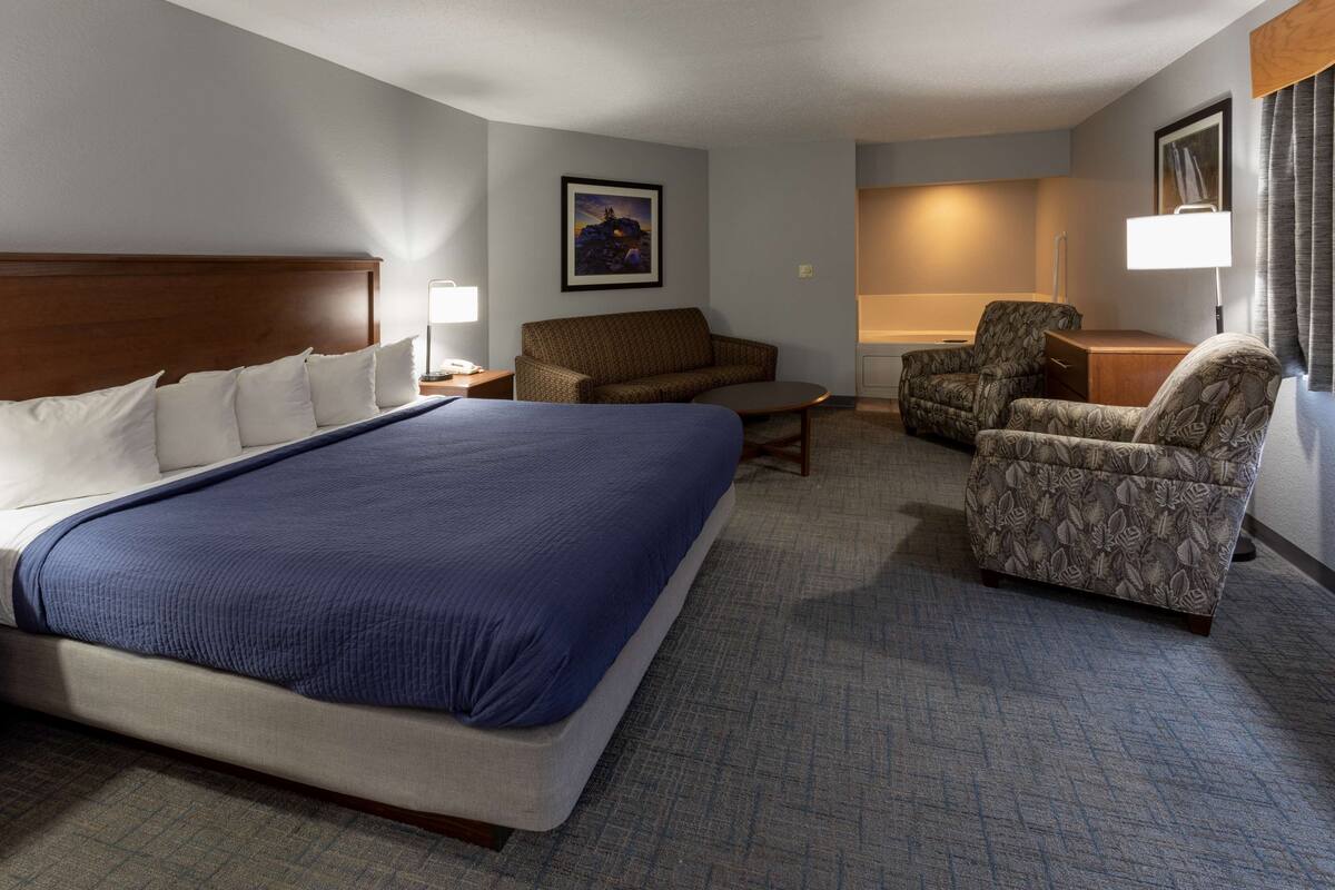 A hotel room with a large bed, a sofa, a chair, and a desk.