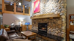 A cozy lobby with a stone fireplace, leather seating, a wooden coffee table, and a desk with a computer. - Black Beach Inn by GrandStay (Silver Bay)