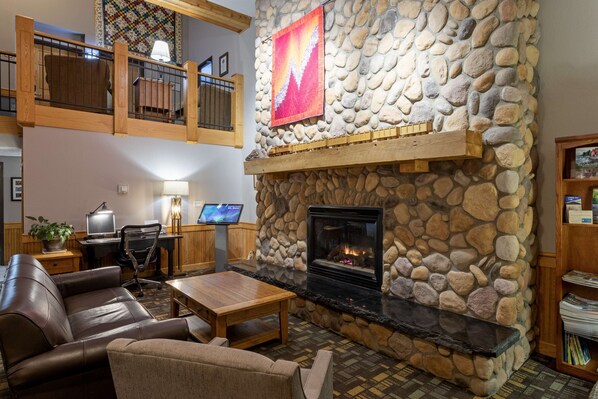 A cozy lobby with a stone fireplace, leather seating, a wooden coffee table, and a desk with a computer.
