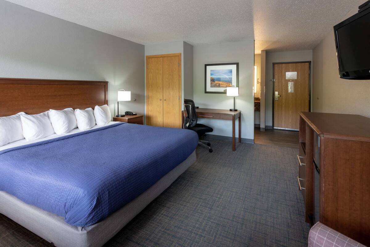 A hotel room with a large bed, a desk, a chair, a TV, and a wardrobe.