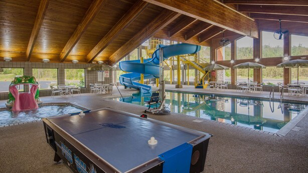 An indoor pool area with a table tennis table, a blue water slide, and a seating area with tables and chairs. - Black Beach Inn by GrandStay (Silver Bay)
