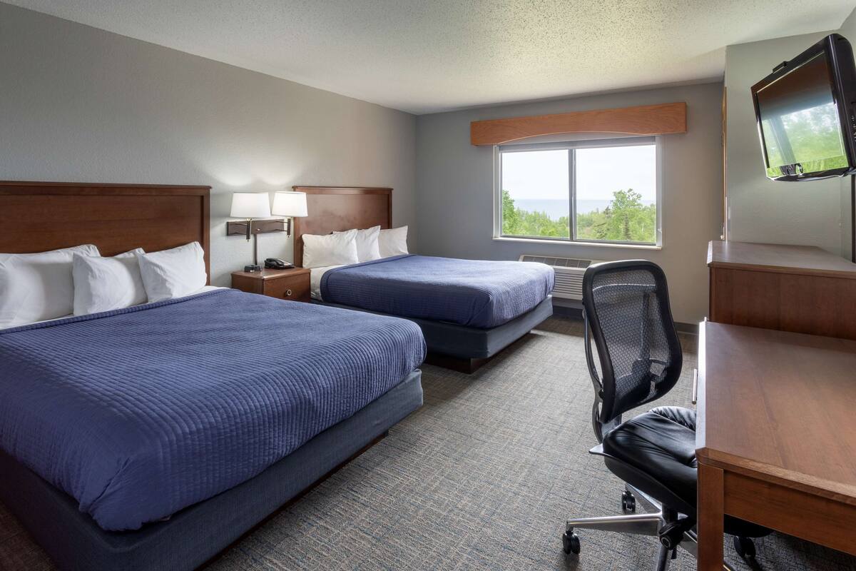 A hotel room with two beds, a desk, a chair, a TV, and a window with a view.