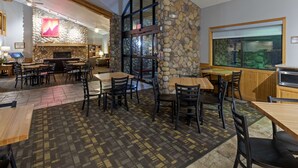 A restaurant with stone walls, wooden tables, and chairs. There is a fireplace and a large window with a view. - Black Beach Inn by GrandStay (Silver Bay)
