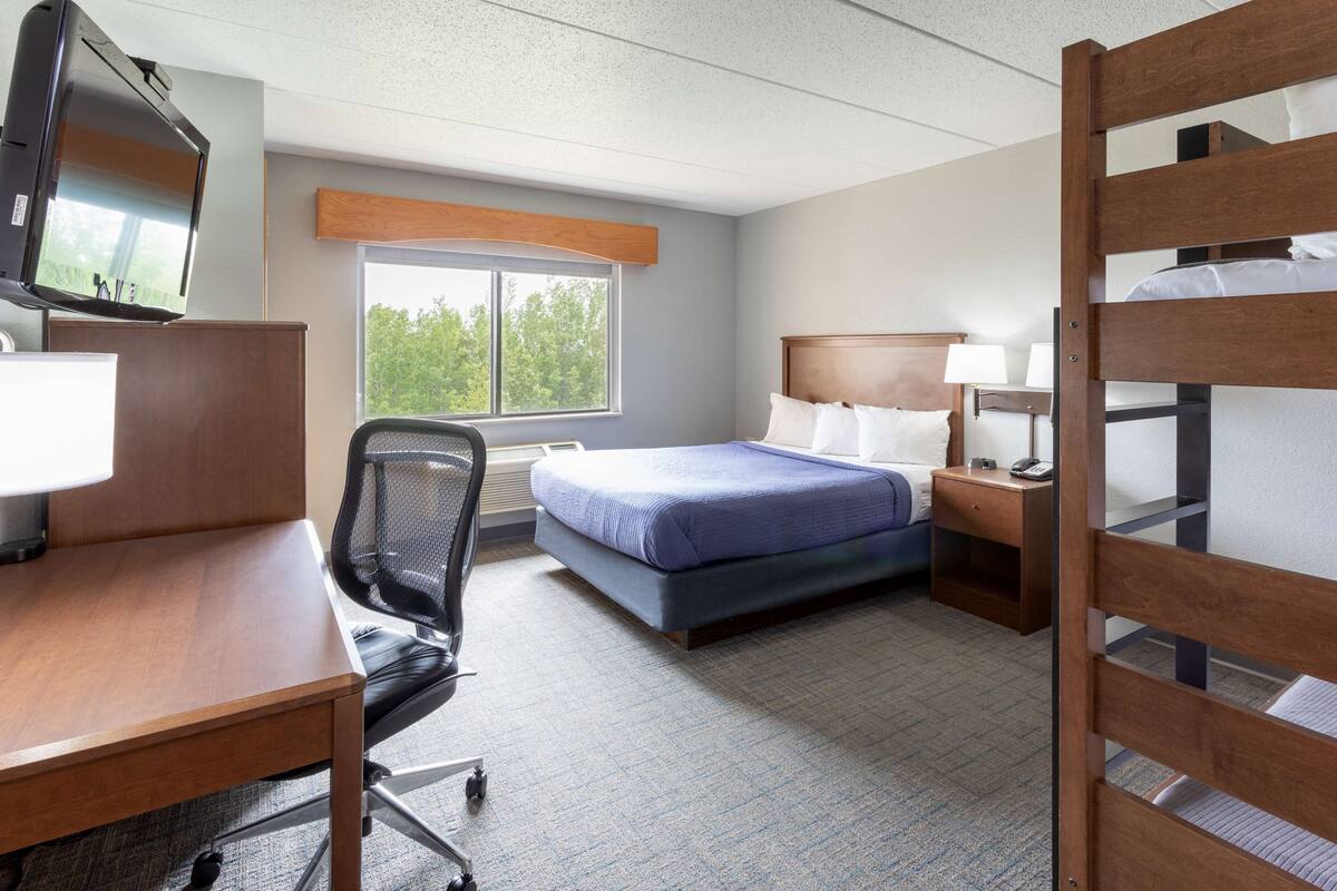 A hotel room with a bed, desk, chair, TV, and window.
