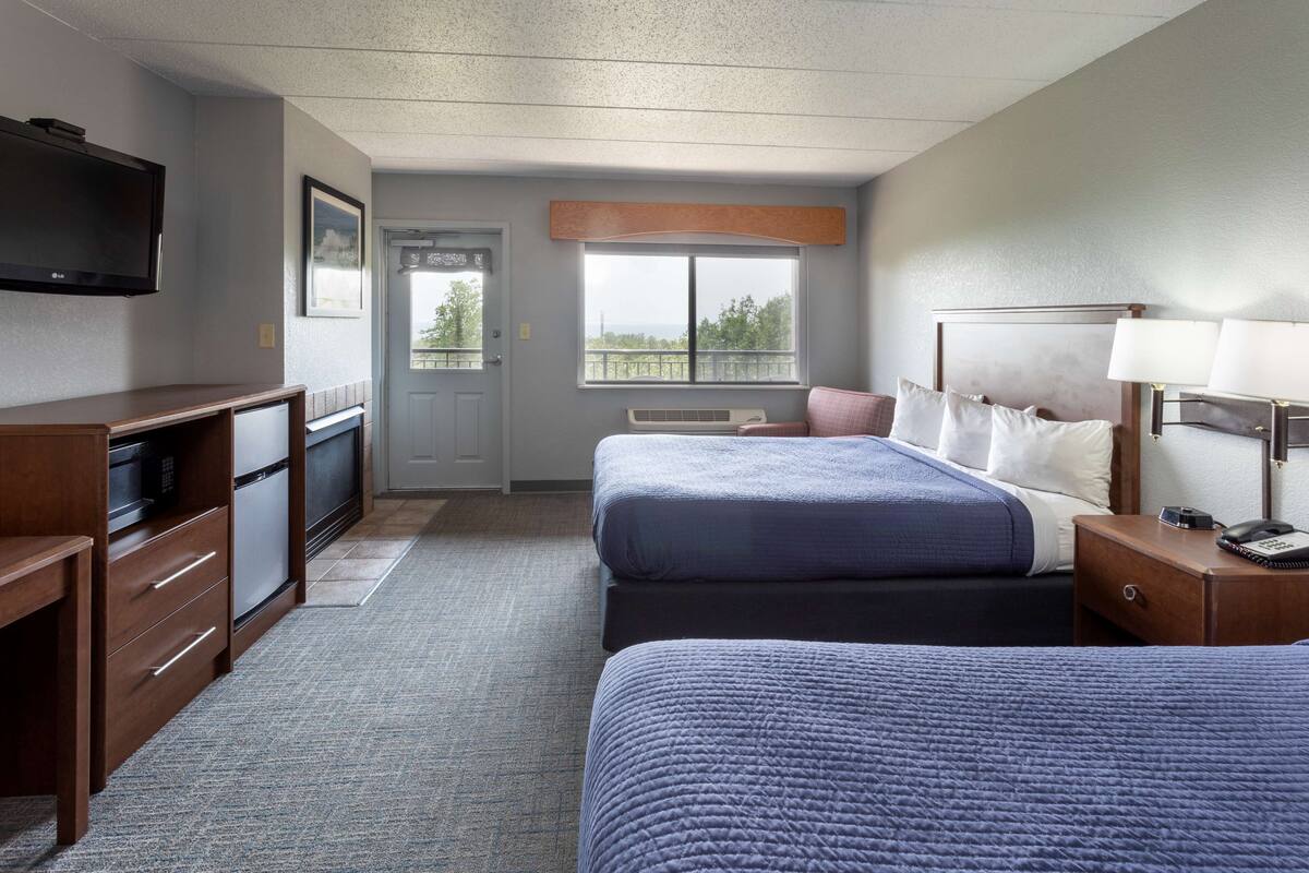 A hotel room with two beds, a TV, a desk, and a window with a view.