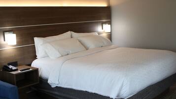A hotel room with a large bed, a bedside table with a phone and remote control, and two wall-mounted lamps.