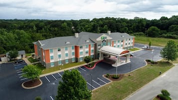 A hotel with a parking lot, a covered entrance, and a view of the surrounding greenery.
