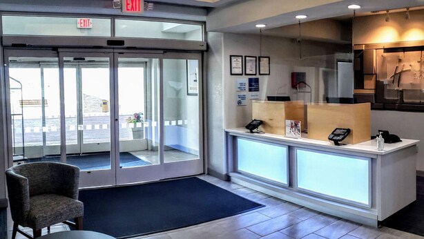 A hotel reception area with a glass door entrance, a reception desk with a phone and a digital display, and a wall-mounted sign. - Holiday Inn Express & Suites Enterprise by IHG (Enterprise)