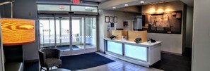 A hotel reception area with a glass door entrance, a reception desk with a phone and a digital display, and a wall-mounted sign. - Holiday Inn Express & Suites Enterprise by IHG (Enterprise)