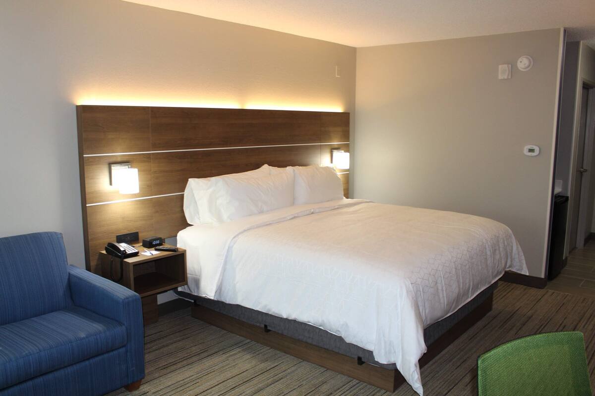 Una habitación de hotel con cama, mesita de noche, lámpara y una silla azul.