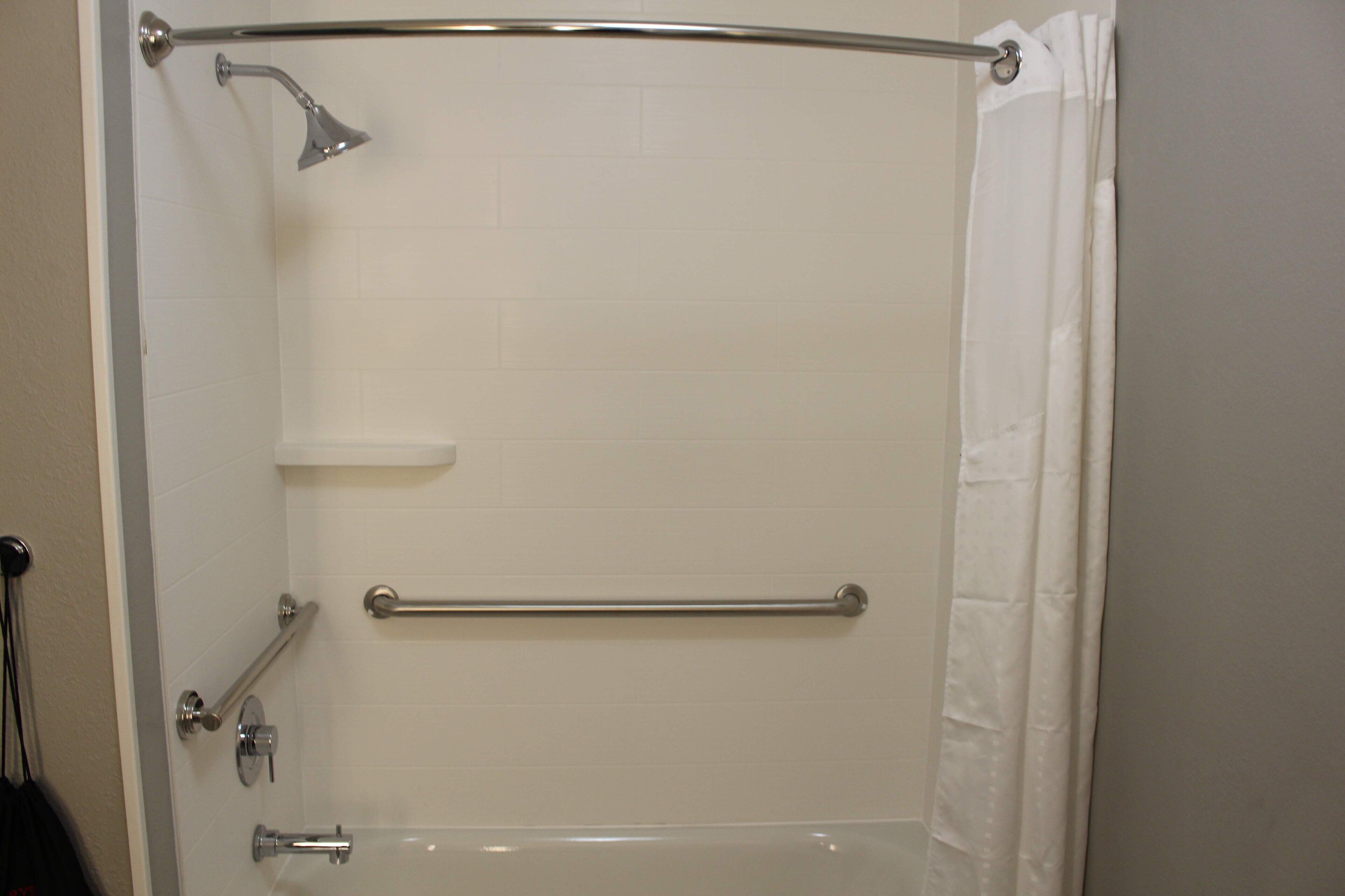 A bathroom with a shower, grab bars, and a white curtain.