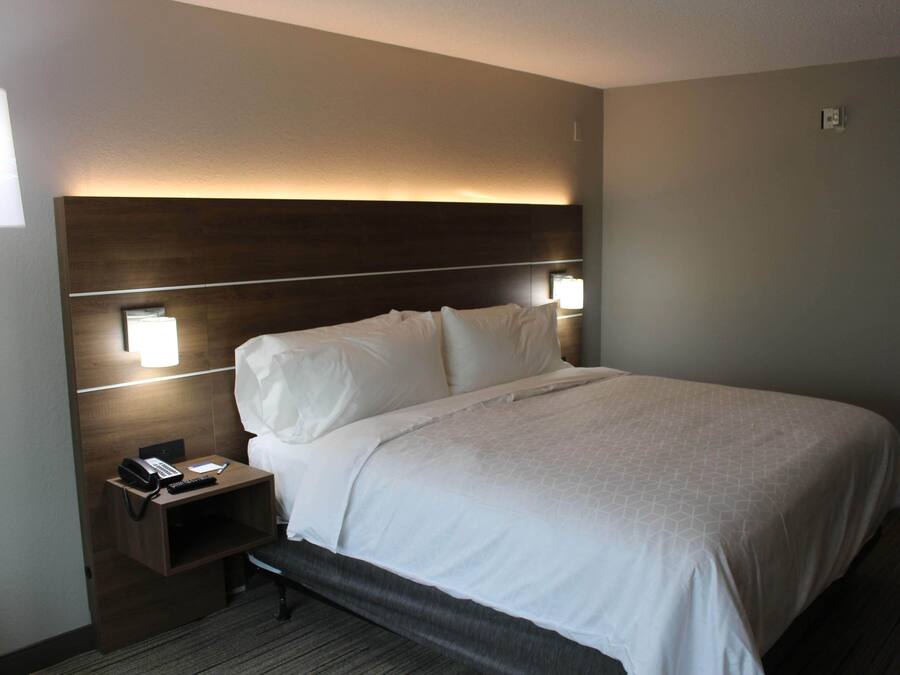 Quarto de hotel com uma cama grande, luminárias de cabeceira, mesa de cabeceira com telefone e controle remoto, e cabeceira com iluminação embutida.