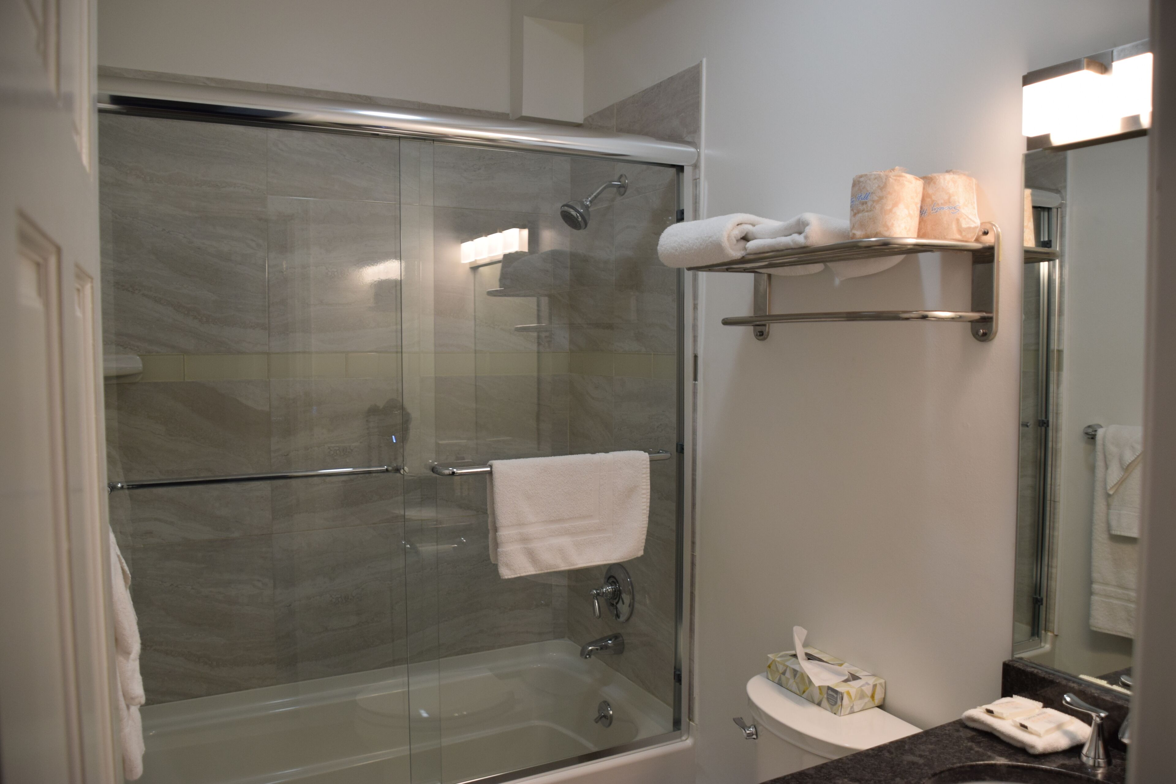 Een moderne badkamer met een douche met glazen wand, een witte wastafel en een spiegel erboven.