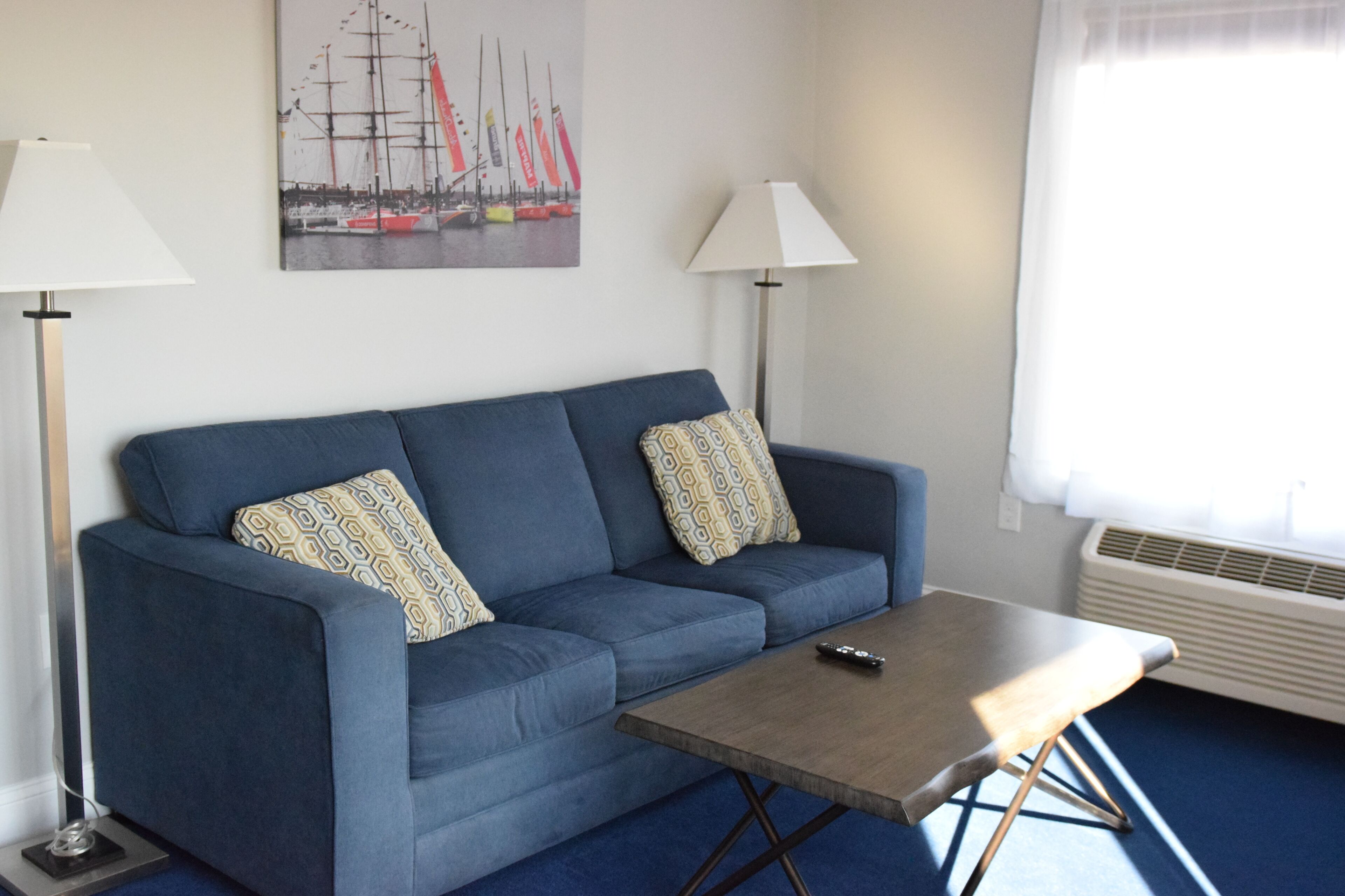 A blue sofa with patterned cushions, a wooden coffee table, and a remote control on it.