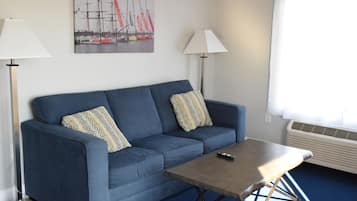 A blue sofa with patterned cushions, a wooden coffee table, and a remote control on it.
