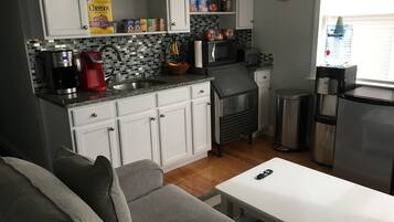 A compact kitchen with white cabinets, a microwave, a coffee maker, and a water dispenser.