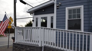 A house with a stone foundation, a white porch railing, and a window with a white frame. - Rhea's Inn By The Sea (Middletown)