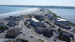 An aerial view of a coastal town with a beach, roads, and buildings.