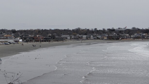 A beach with a long stretch of sand and a few buildings in the background. - Rhea's Inn By The Sea (Middletown)