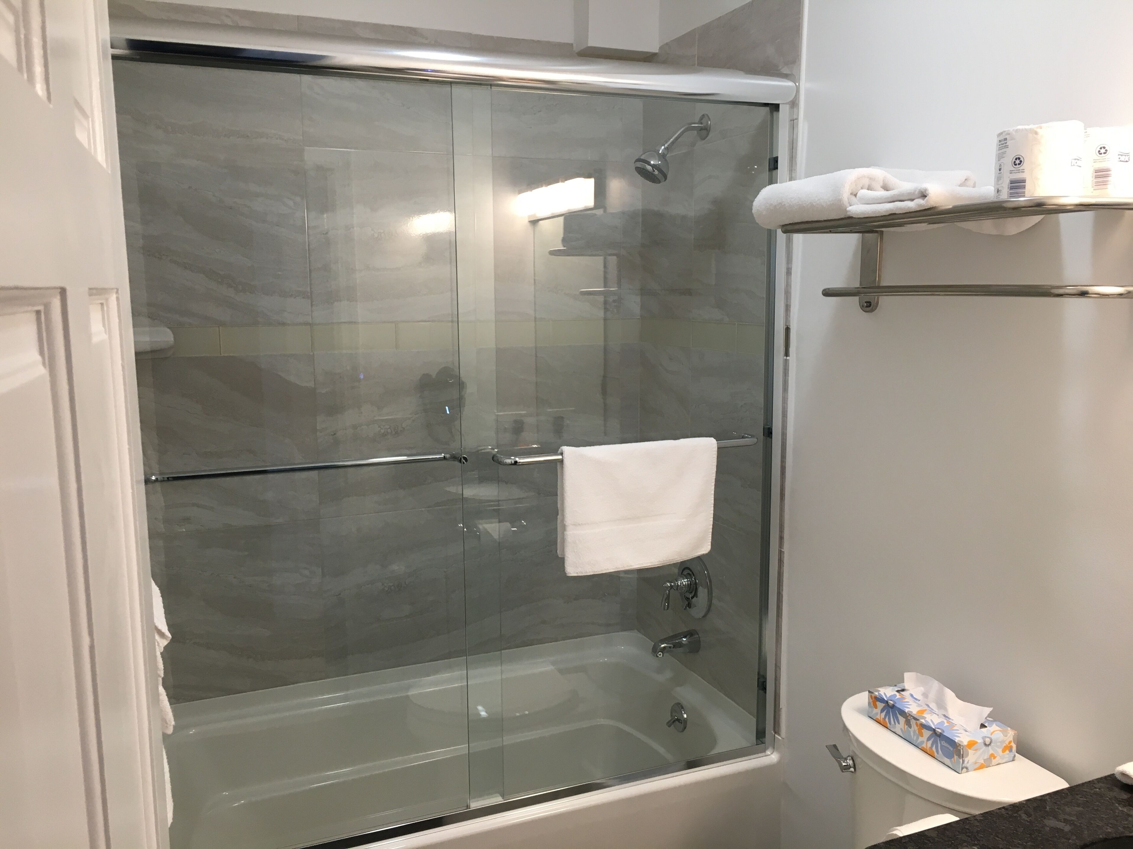 Un baño moderno con ducha de vidrio, inodoro blanco y lavamanos con una toalla y pañuelos en la encimera.