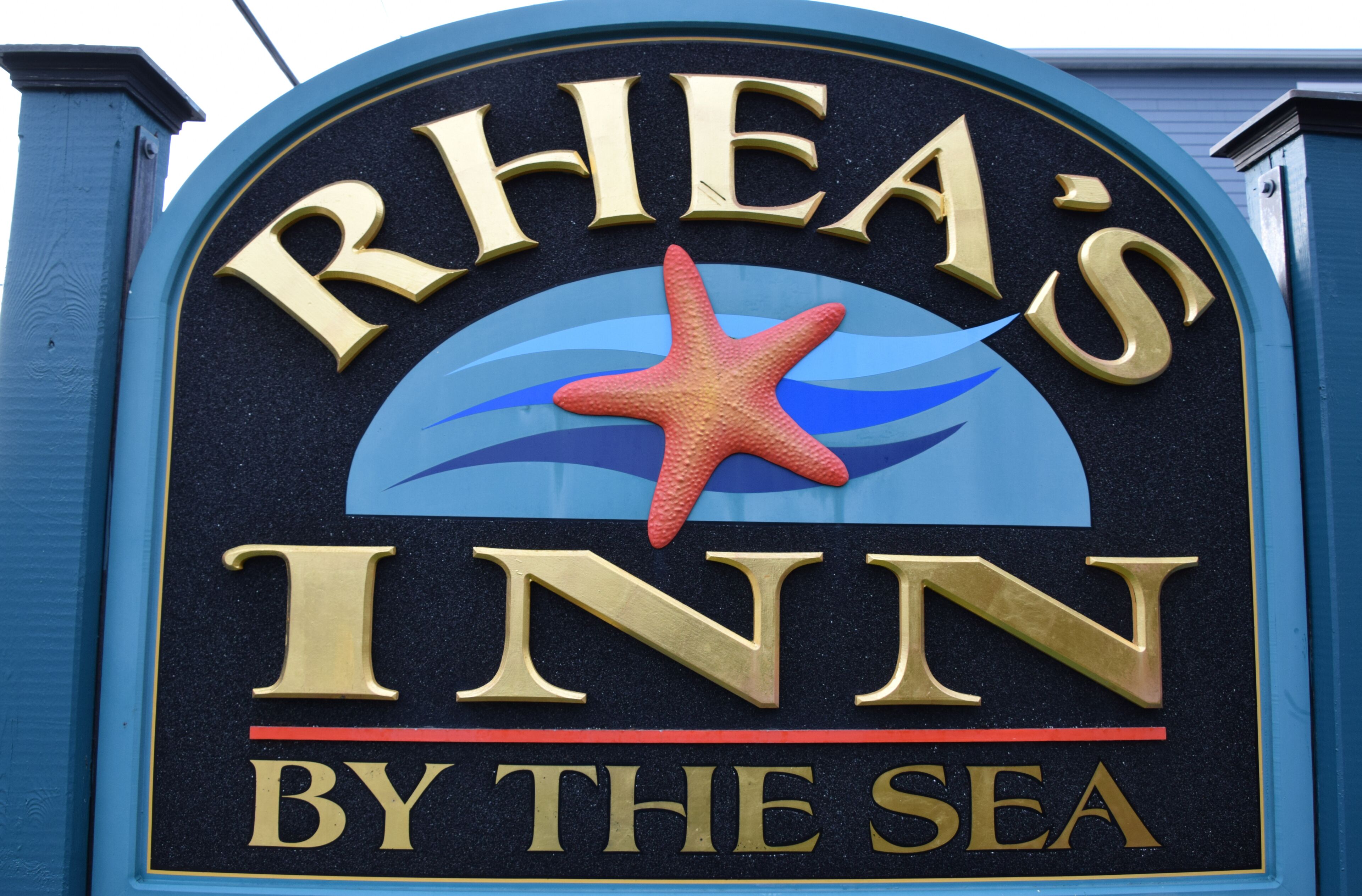 A sign for "Rhea's Inn By The Sea" with a starfish and waves design.
