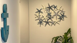 A hallway with a wall-mounted starfish decoration, a potted plant, and a blue carpet. - Rhea's Inn By The Sea (Middletown)