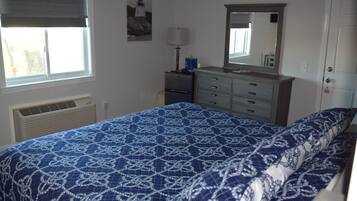 A bedroom with a bed, a dresser, a mirror, a window, and a heater.
