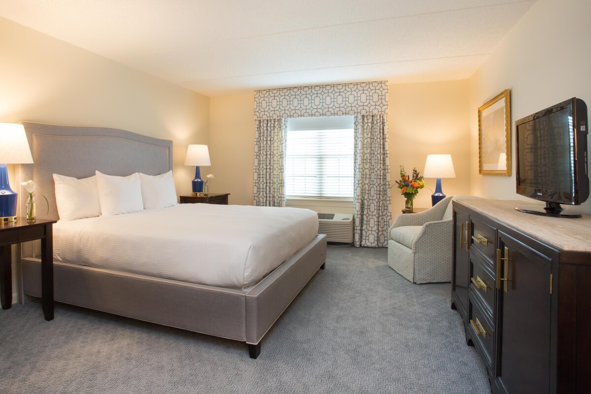 A hotel room with a large bed, two bedside tables with lamps, a TV, a desk, and a chair.