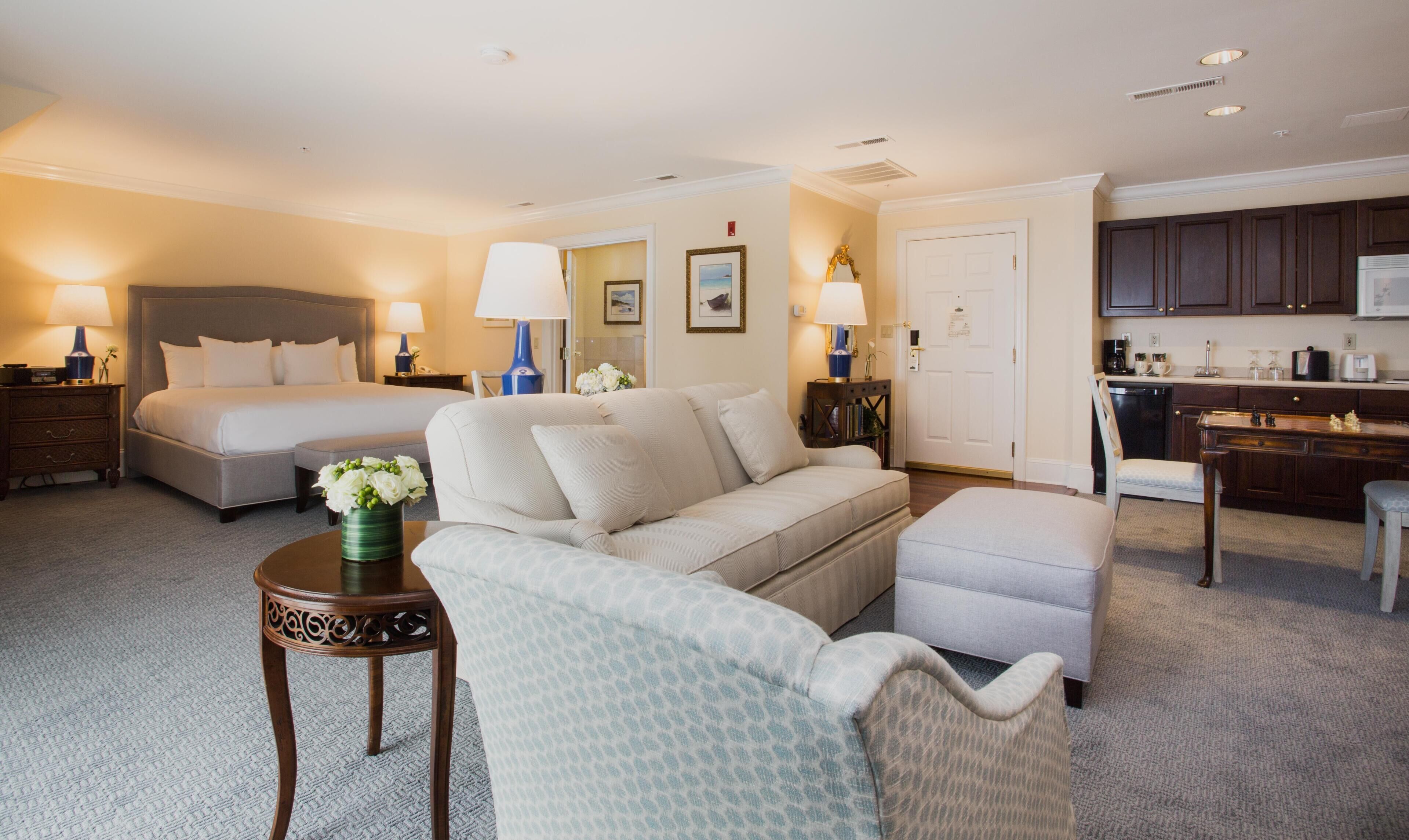 A hotel room with a bed, a sofa, a chair, a small table, and a kitchenette.