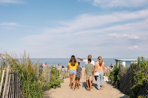 A sandy beach path with people walking, a wooden fence, and a clear sky.