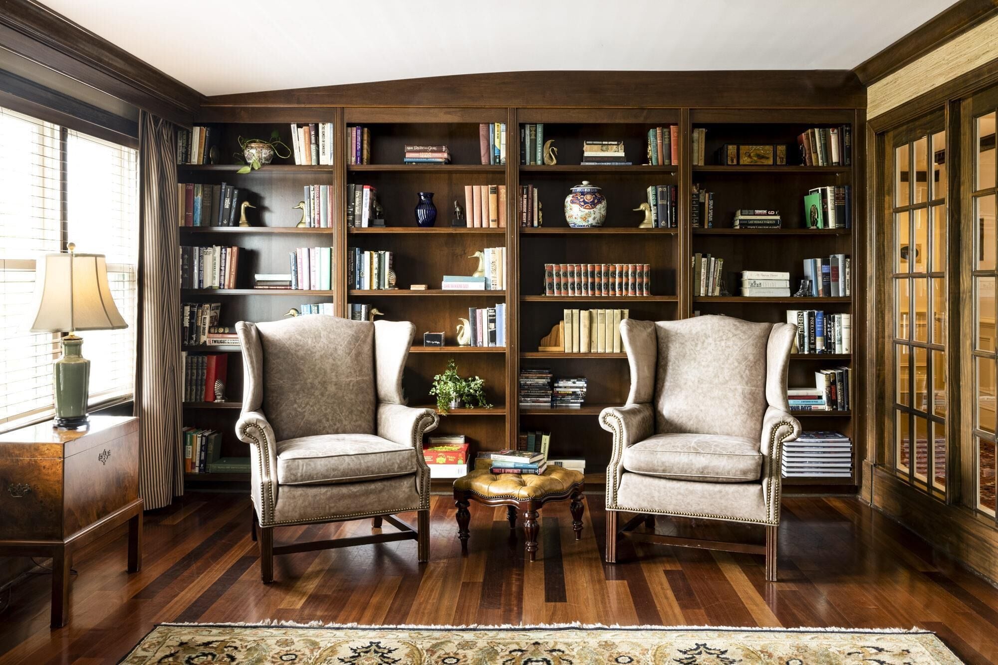 A library with two armchairs, wooden bookshelves, and a patterned rug.